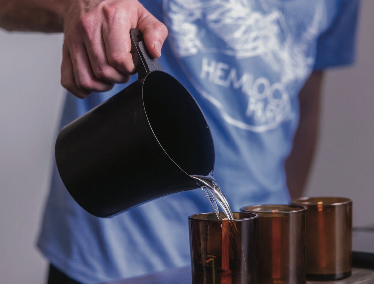Maker pouring coconut apricot wax into amber glass jars with wood wicks, showcasing the Hemlock Park plant-based candle crafting process