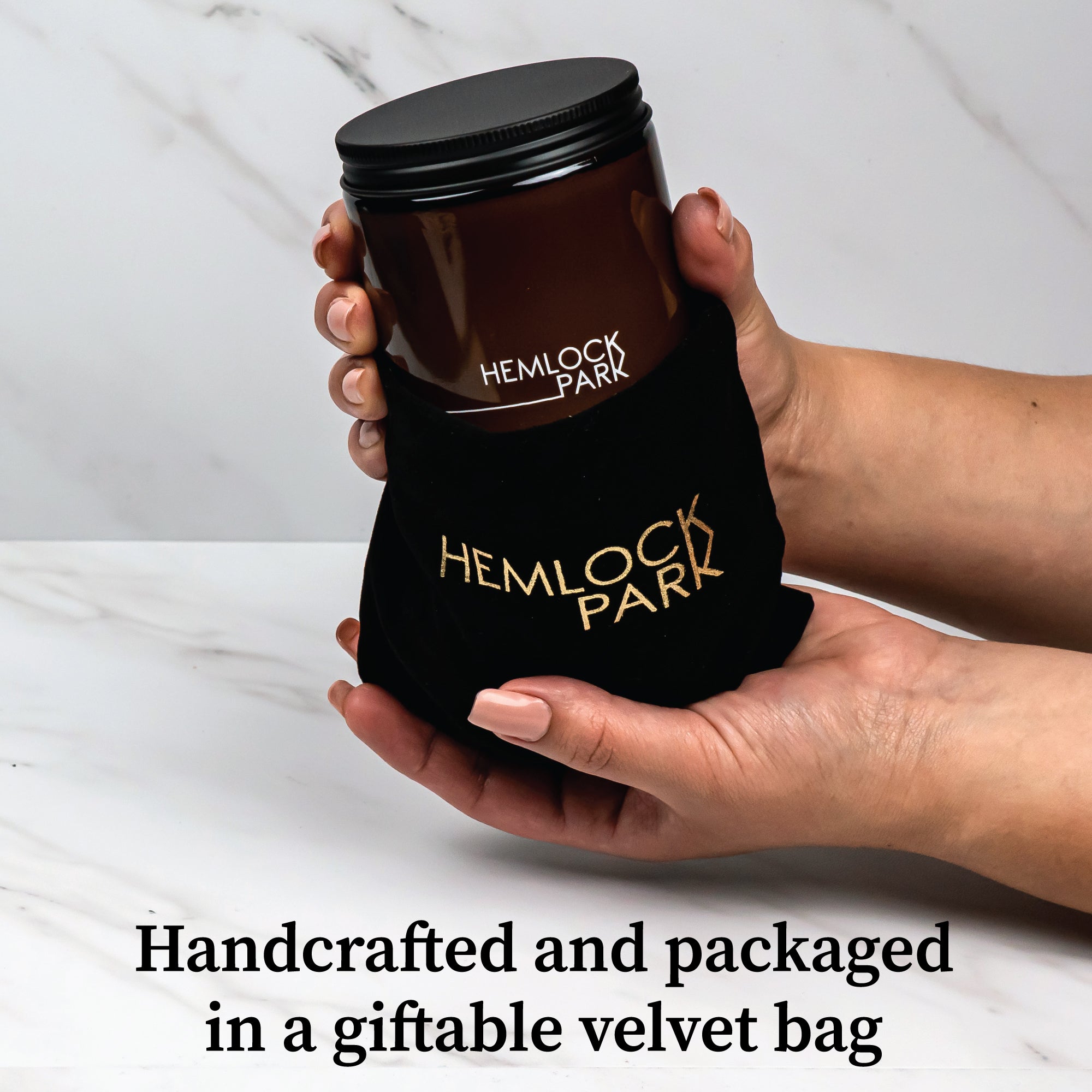 Hemlock Park Sierra Solstice candle in an amber glass jar, held in a black velvet gift bag with gold logo branding.